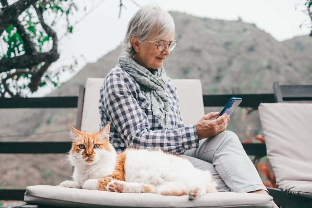 Defocused senior woman sitting outdoors on a chaise longue in the company of her beautiful cat